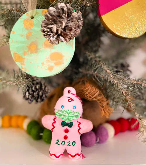 An ornament of a gingerbread man wearing a face mask hangs from a tree